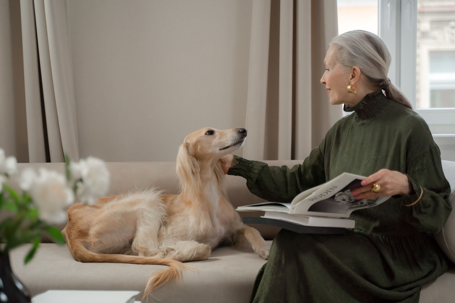 An older woman reading on a sofa with her dog