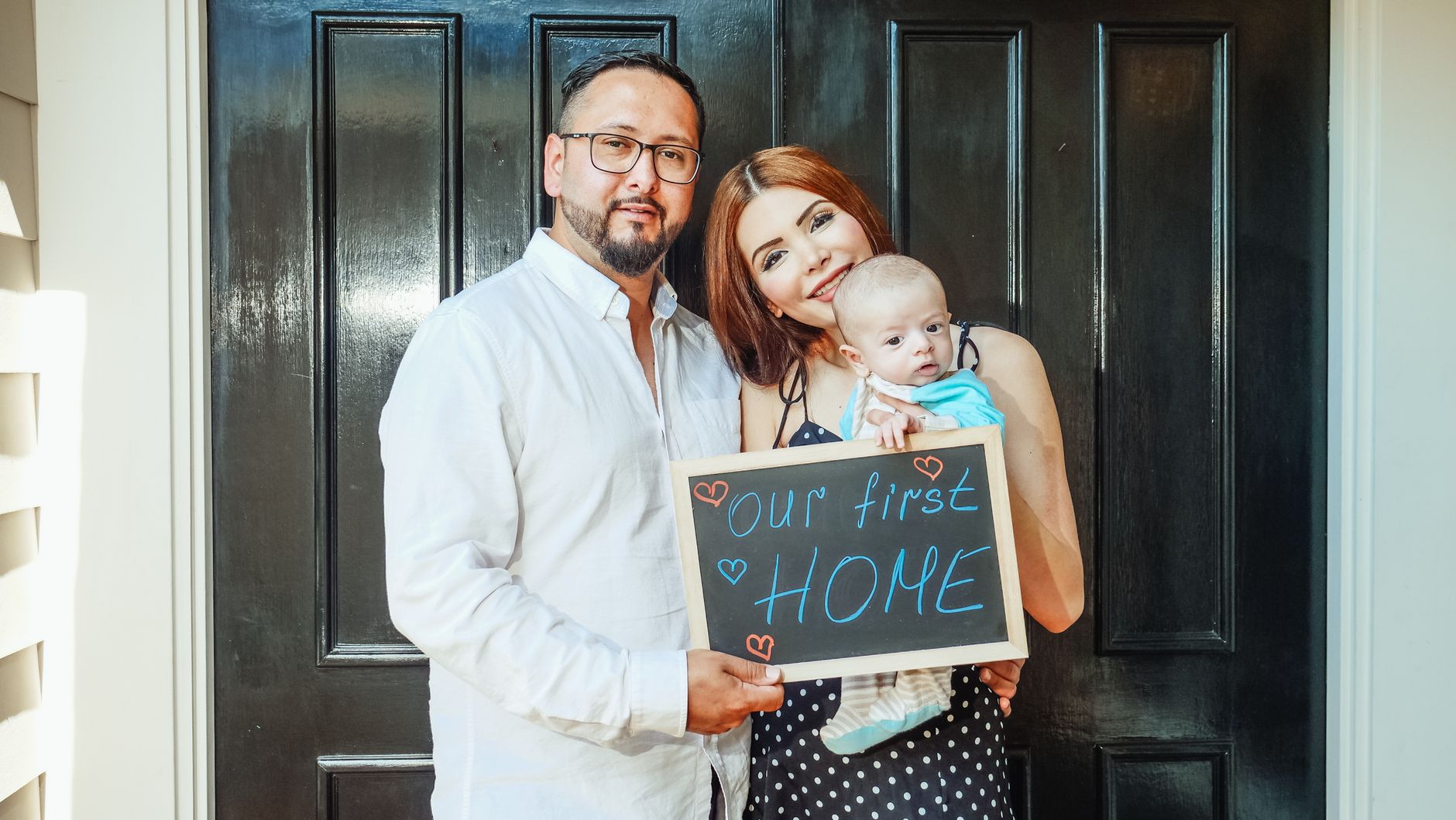 A couple with a baby holding an our first home sign