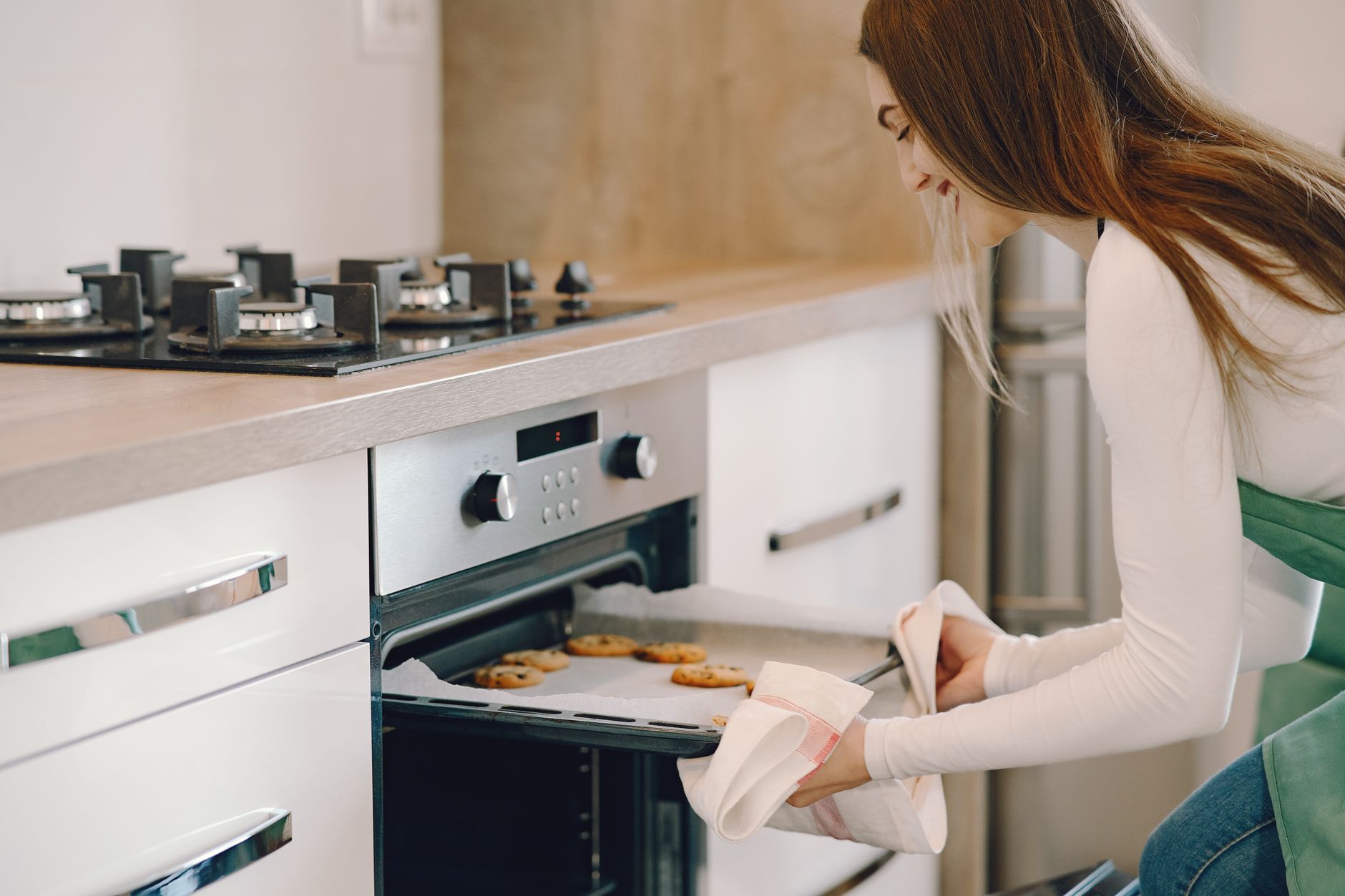A woman taking cookies out of the oven with a towel