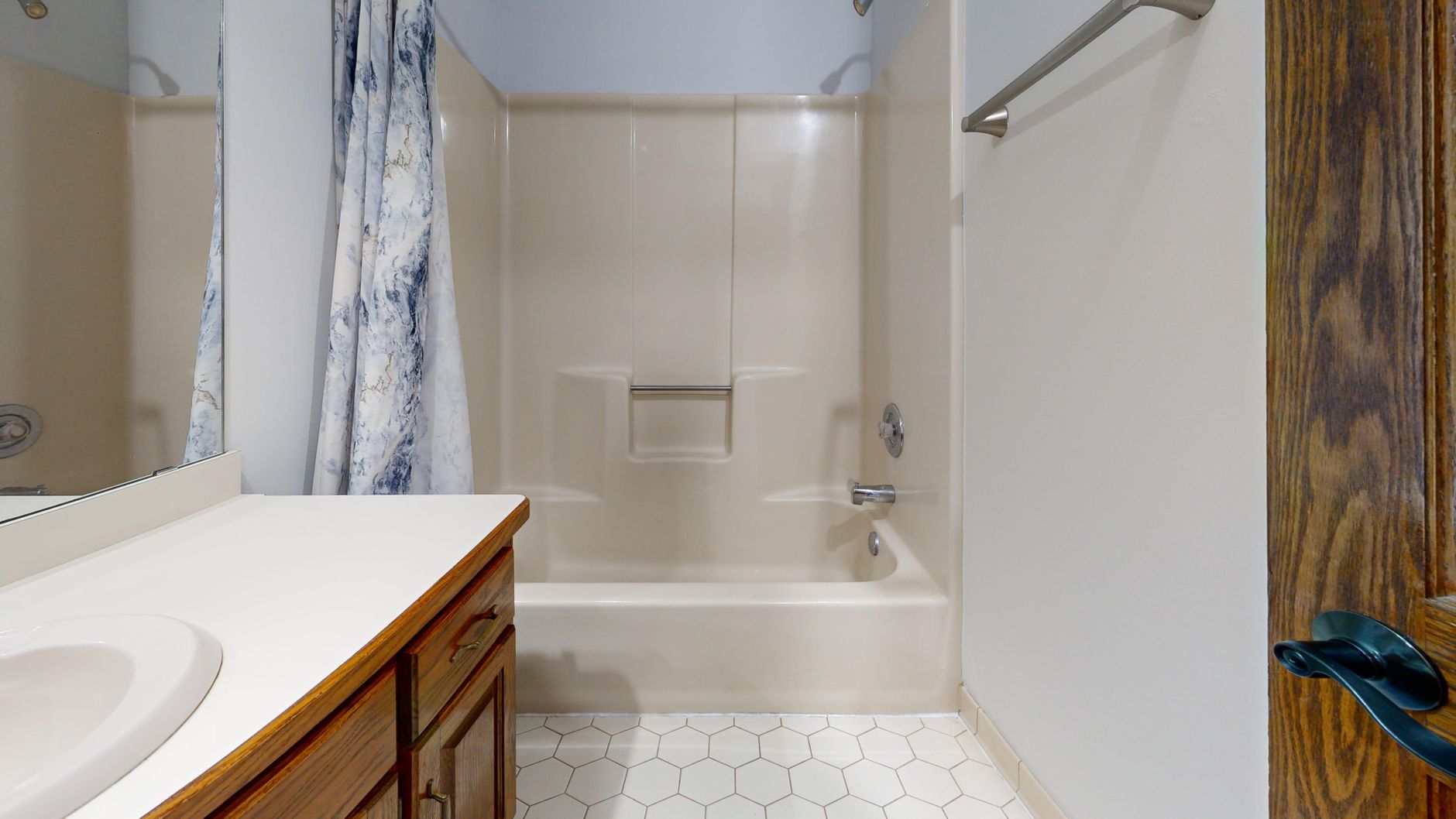 A tub and shower with a curtain beside a wood vanity