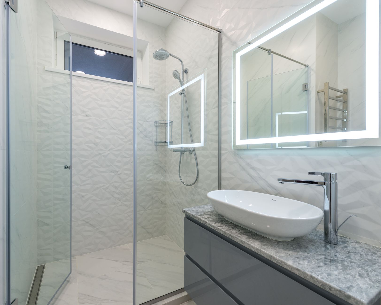 A glass shower and vessel sink with a lit mirror