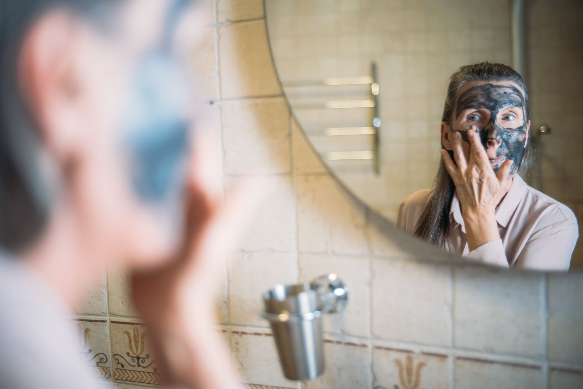 A woman applying a face mask at a bathroom mirror