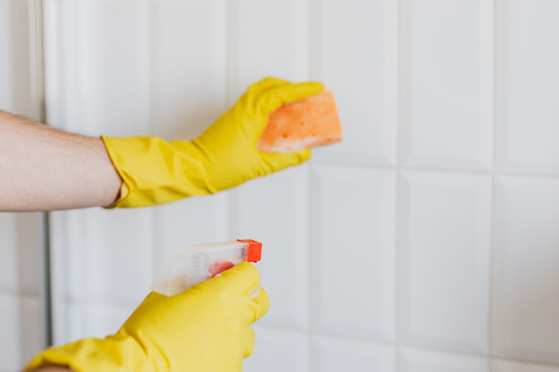 Gloved hands spraying and scrubbing tile