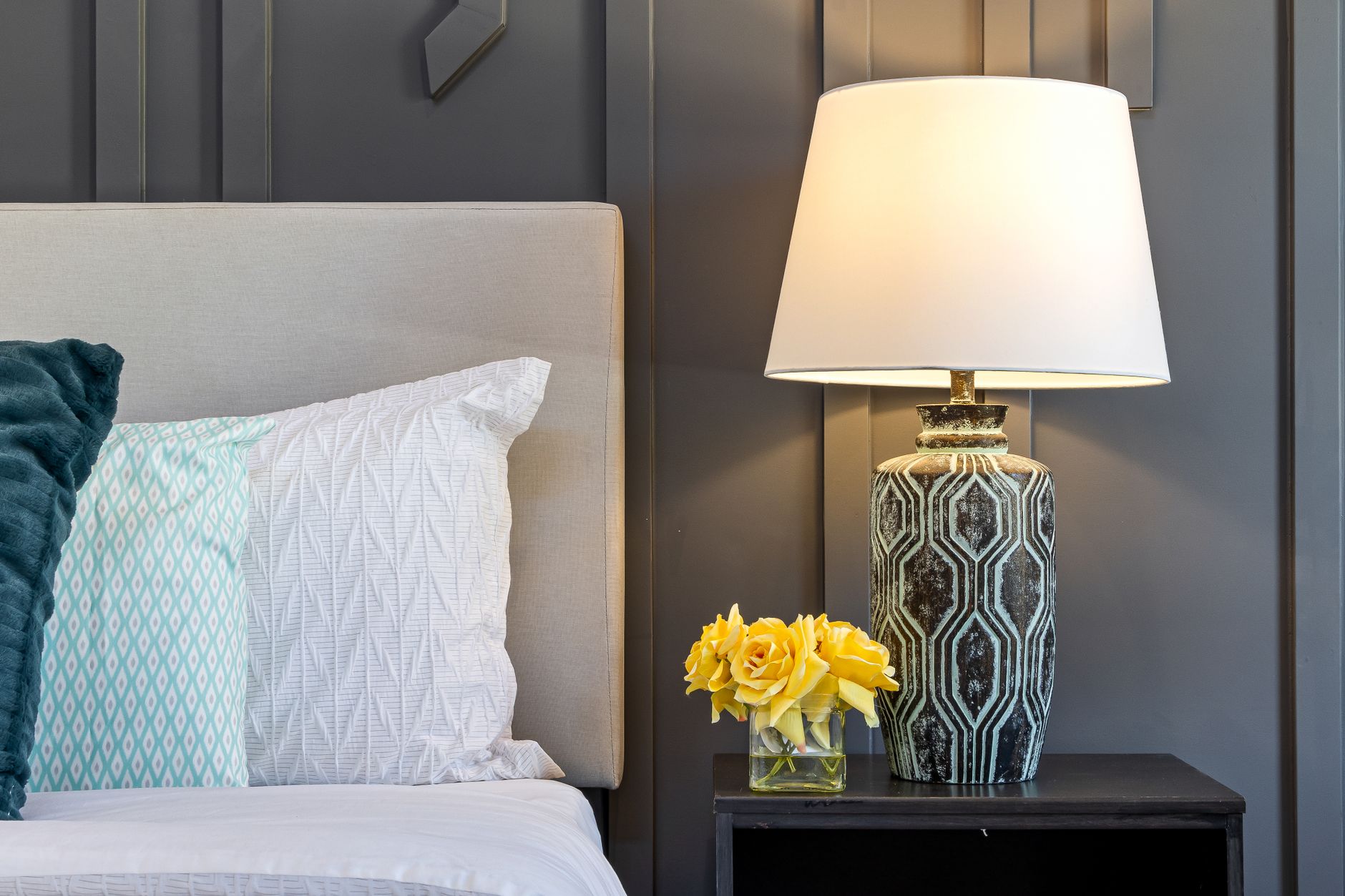 A bedside table with a lamp and yellow flowers