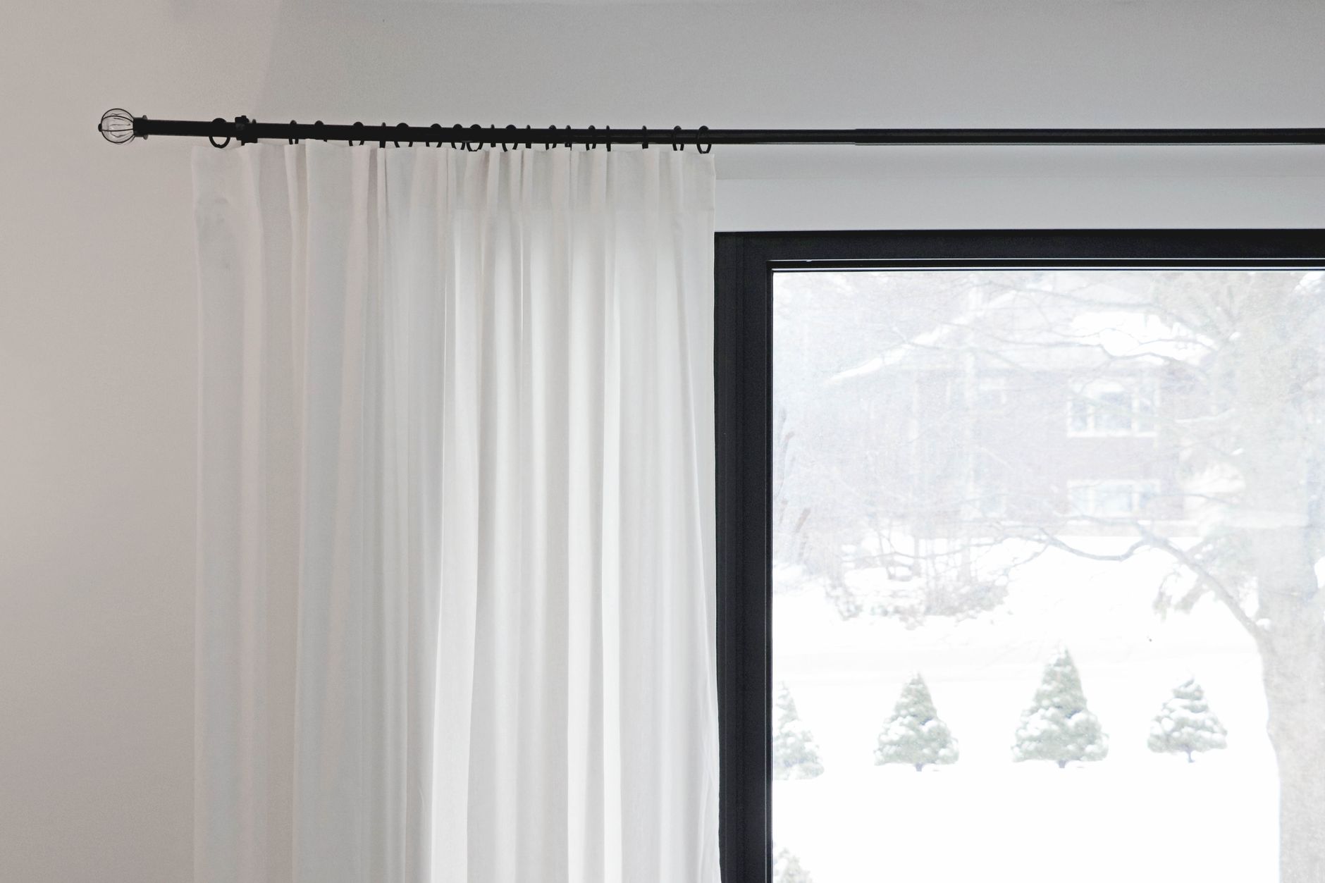 White curtains on a rod by a snowy window