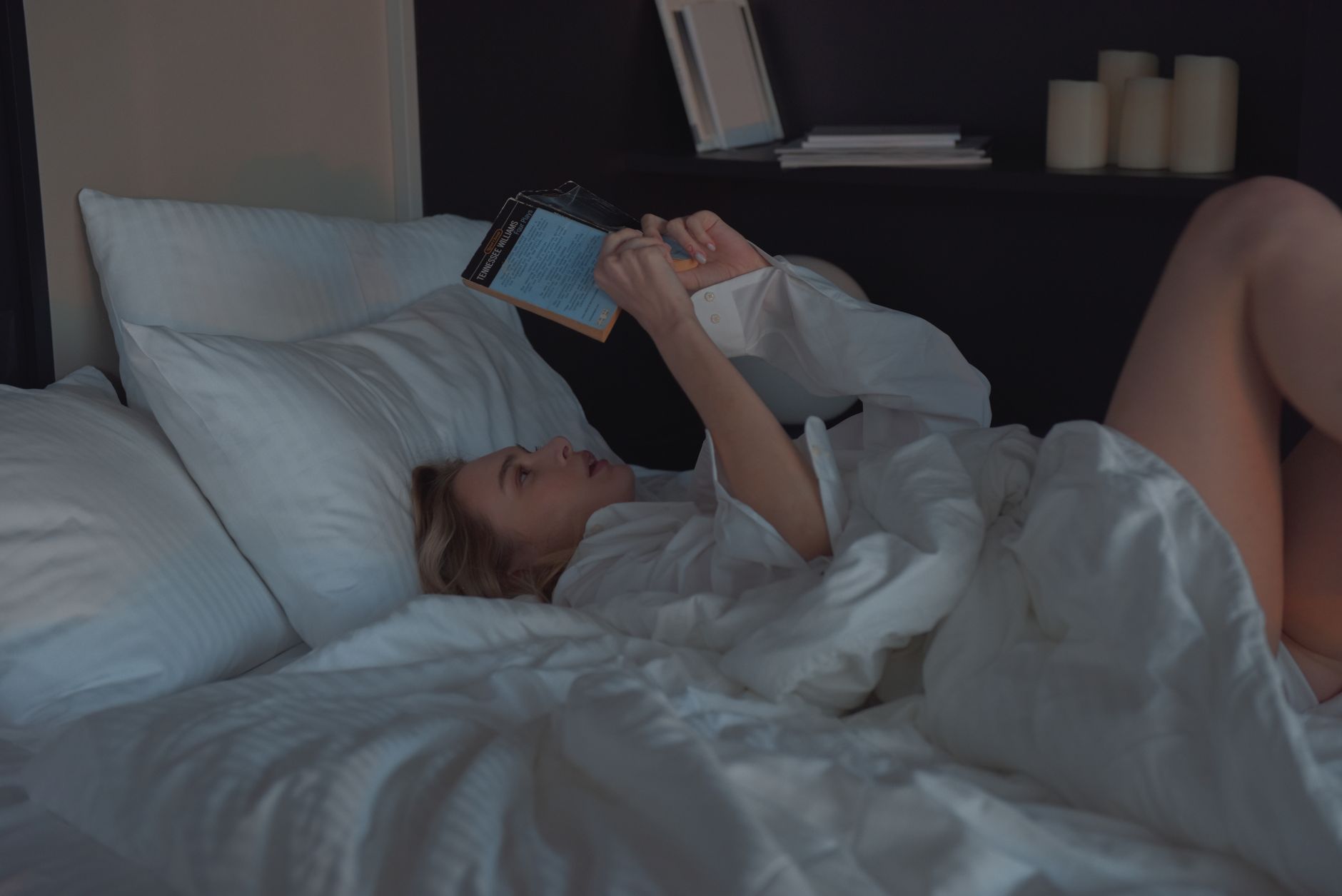 A person reading a book in bed in a dark room