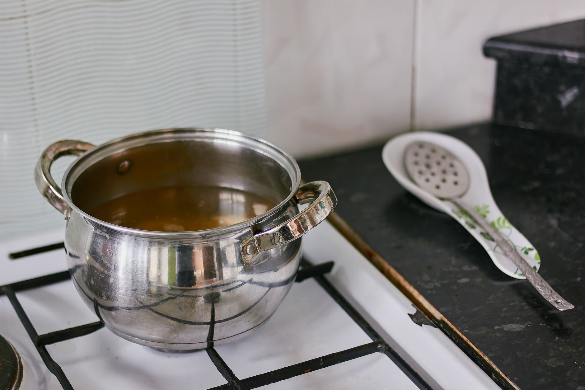 A pot on a gas stove beside a spoon