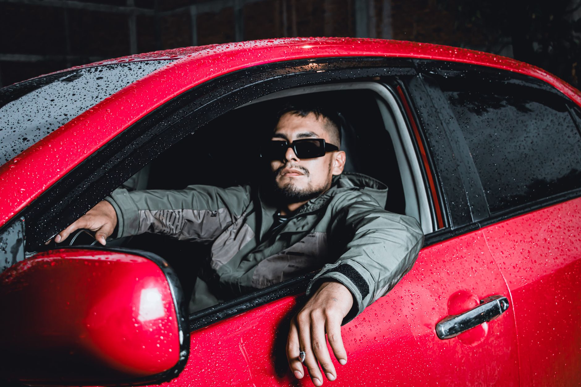 A man leaning out of a red car window in the rain