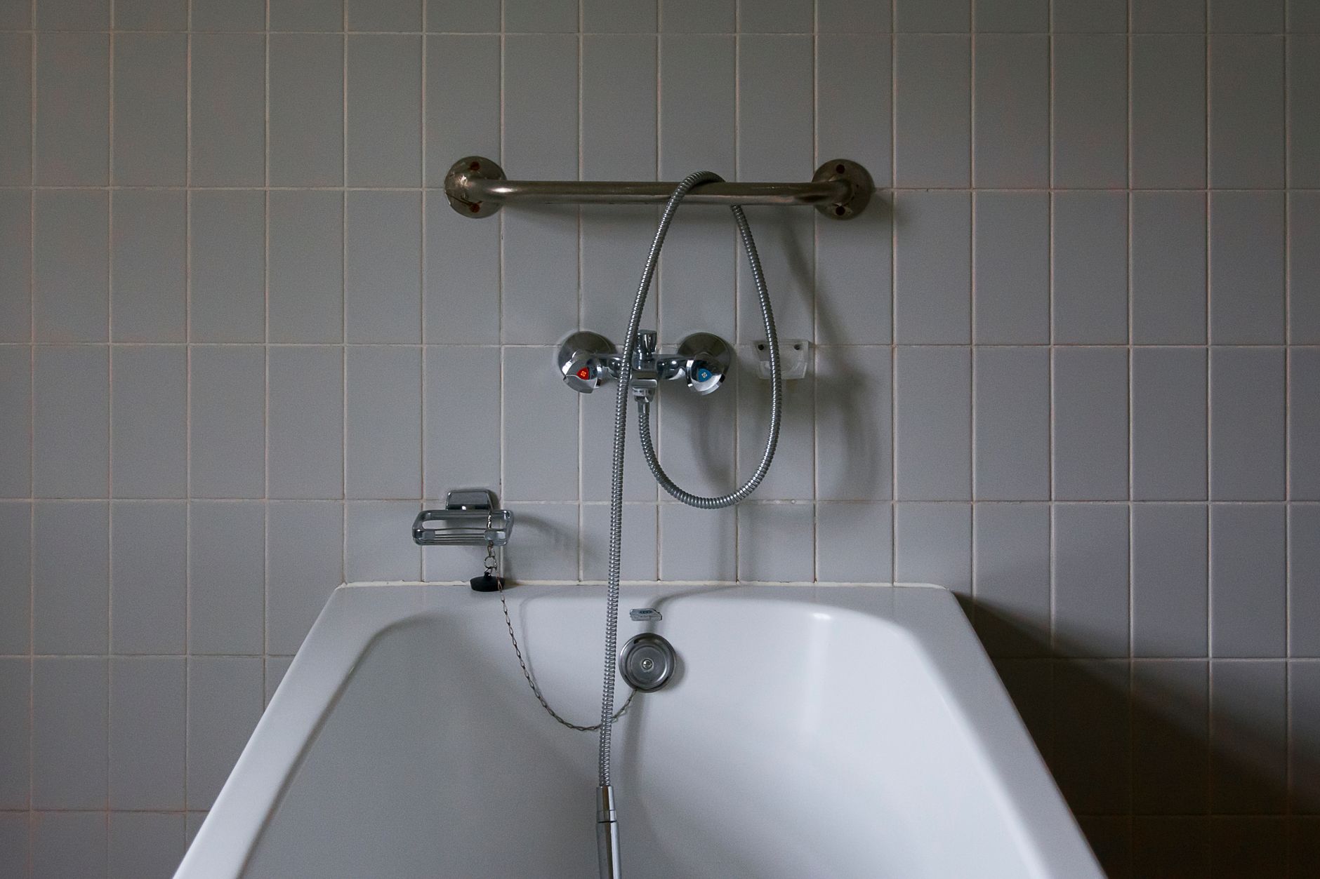 A white bathtub below a tiled wall with a hand shower