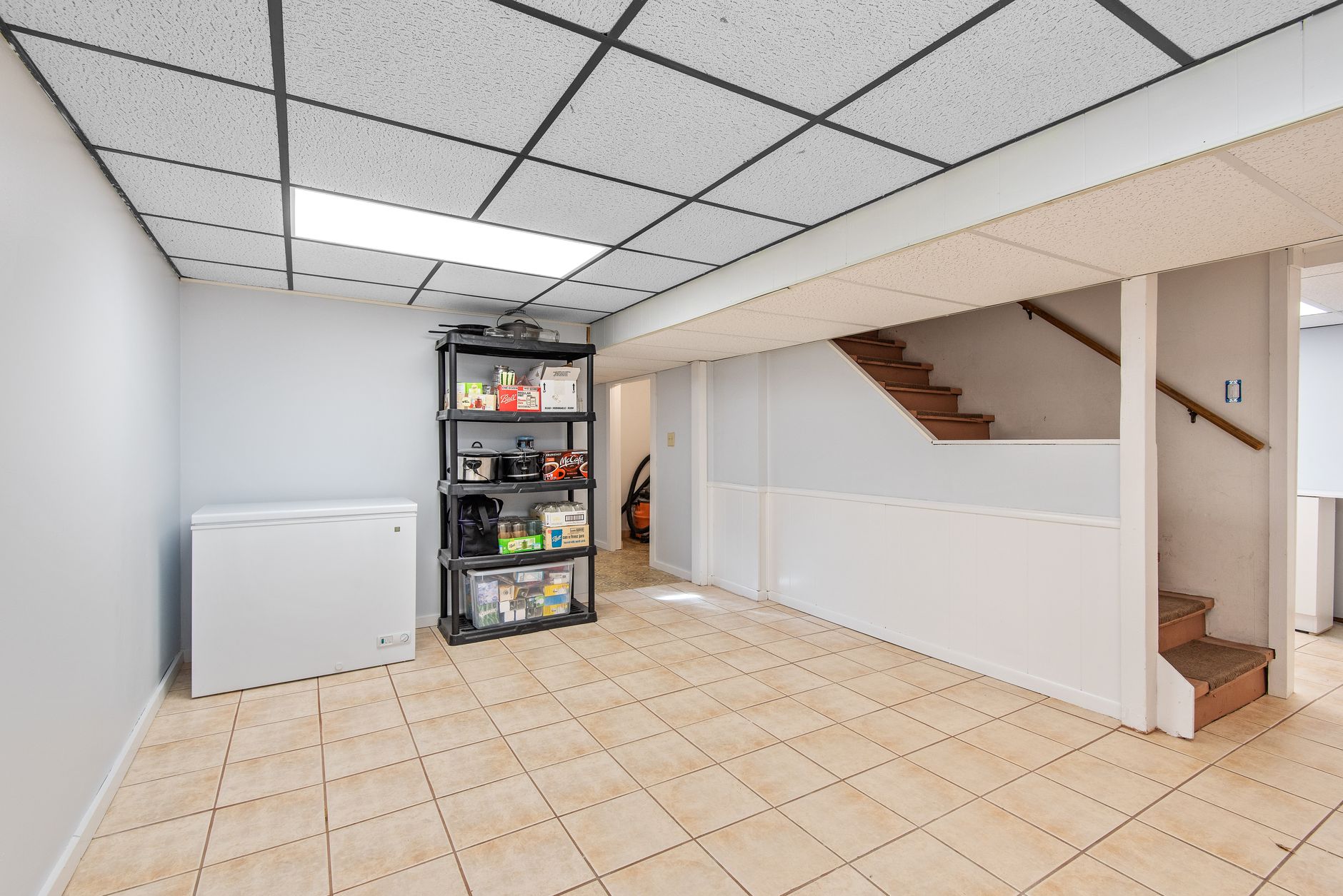 A finished basement with a chest freezer and shelving