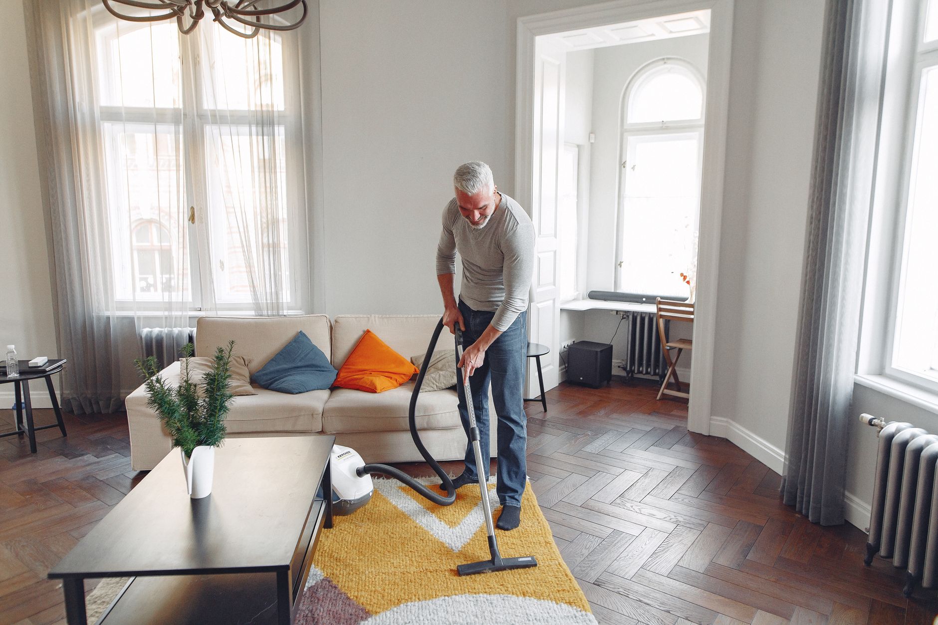 A man vacuuming a rug in a bright living room