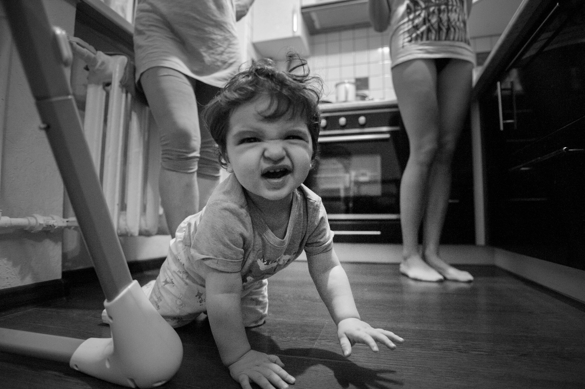 A toddler crawling on a kitchen floor while adults stand nearby