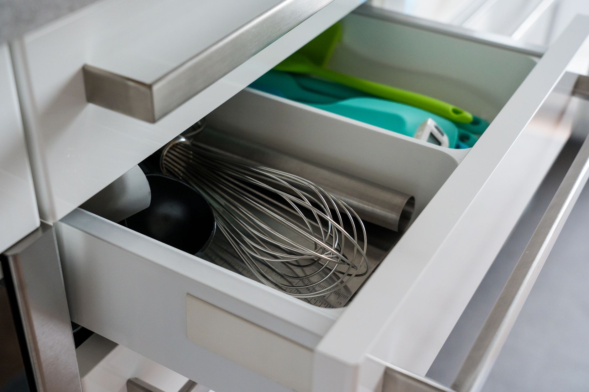 An open kitchen drawer holding a whisk and utensils