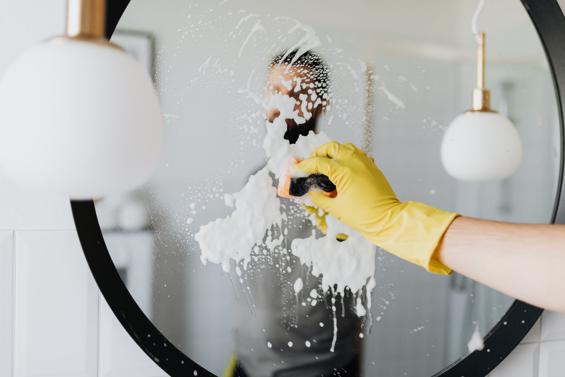 A gloved hand cleaning a round mirror