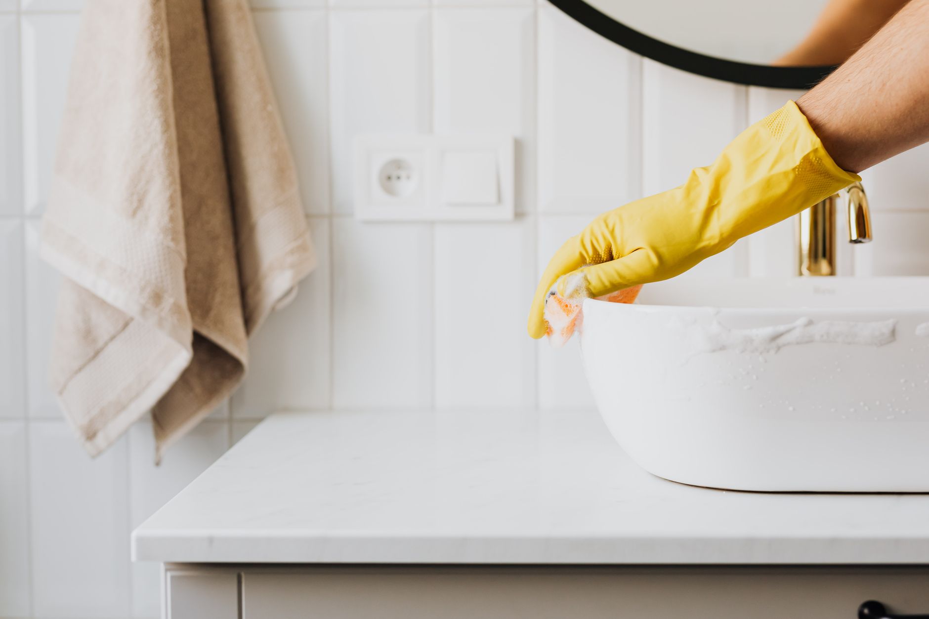 A gloved hand cleaning a bathroom sink