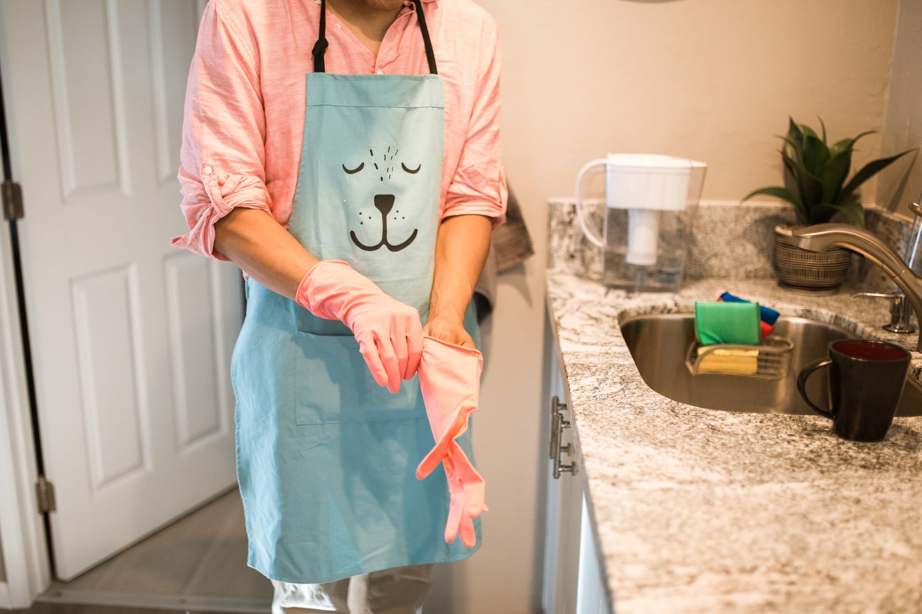 A person pulling on pink rubber gloves in a kitchen
