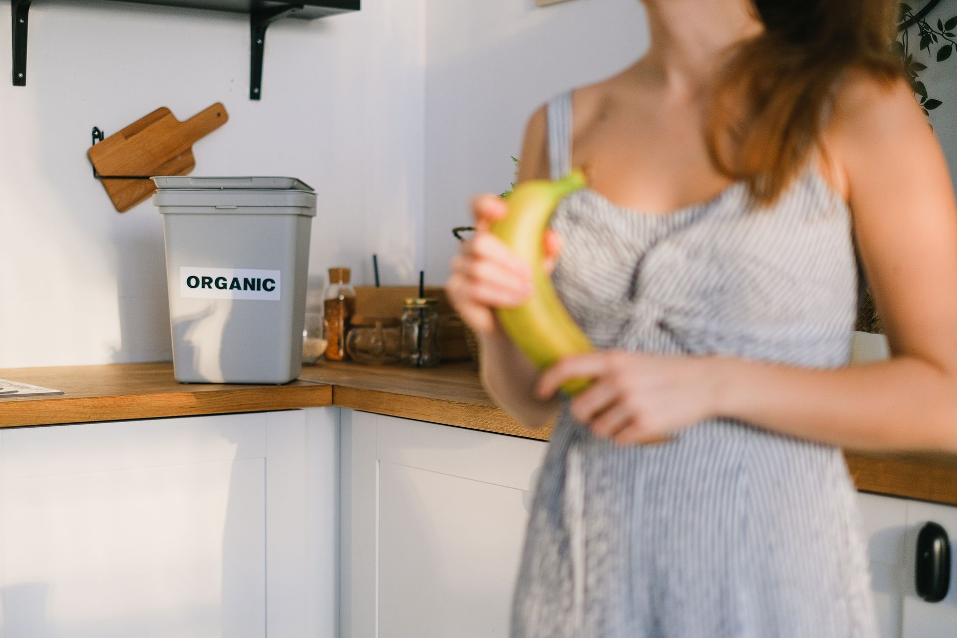 A woman holding a banana by a kitchen compost bin