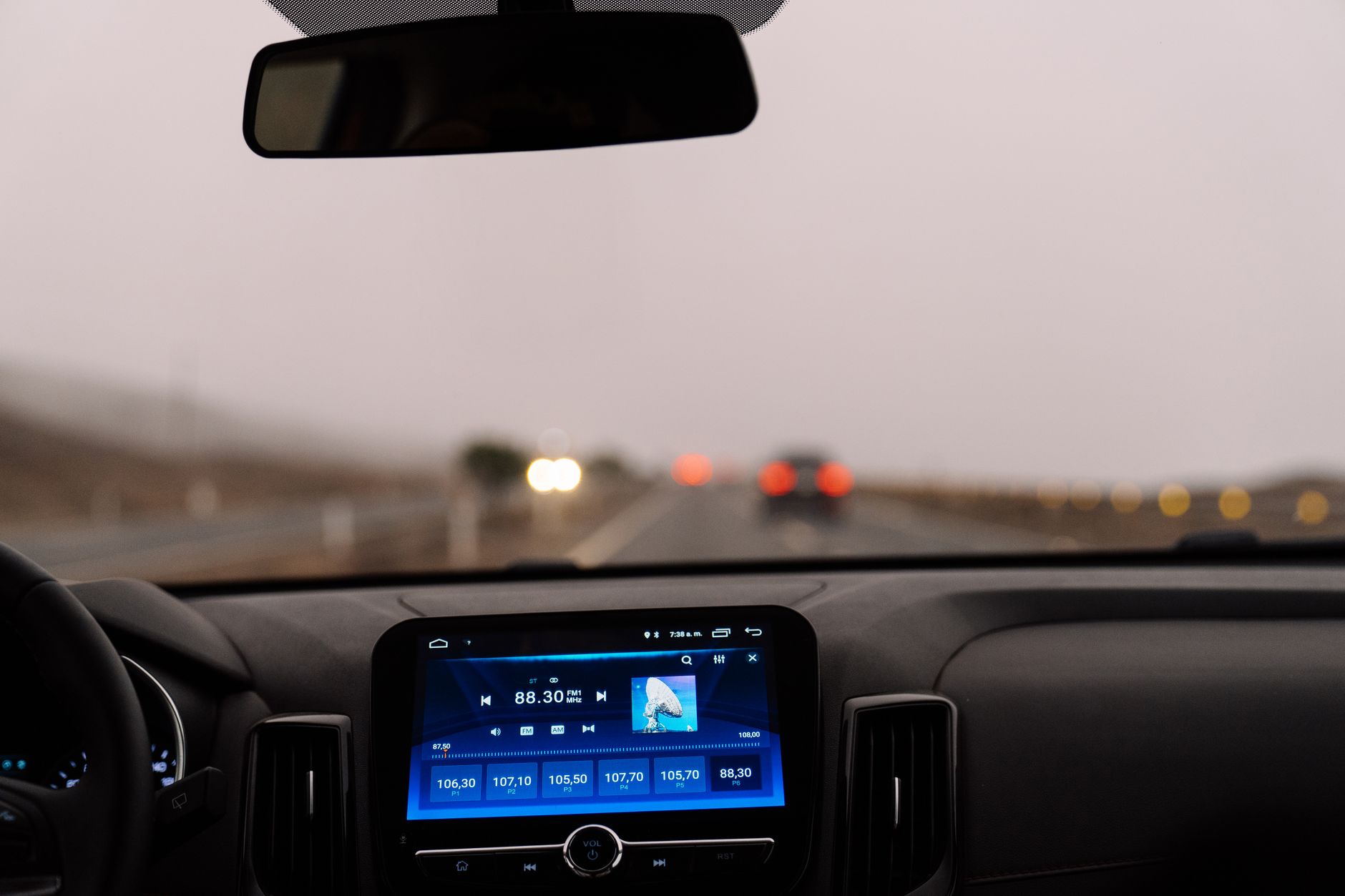 A dashboard screen and rear view mirror on a misty highway