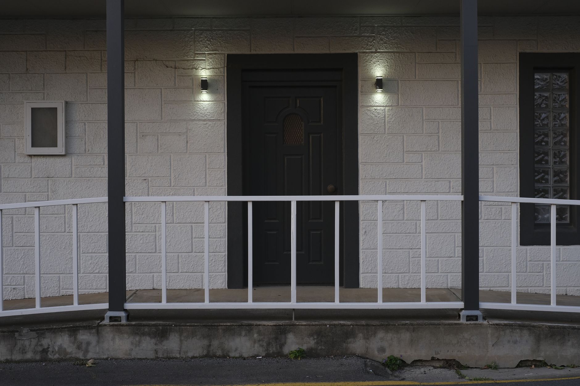 A front porch with wall lights beside a dark entry door