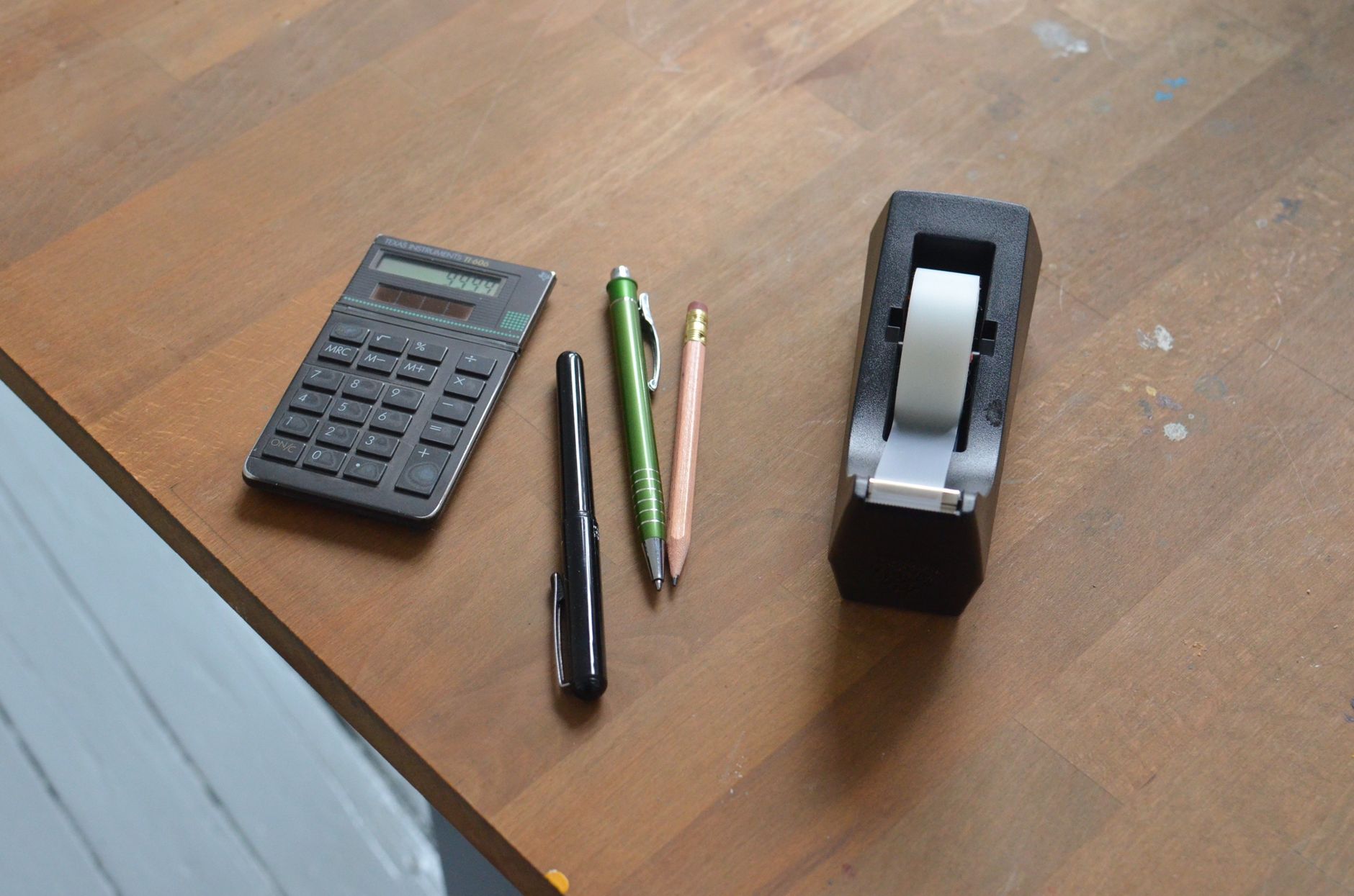 A calculator, pens and tape dispenser on a desk