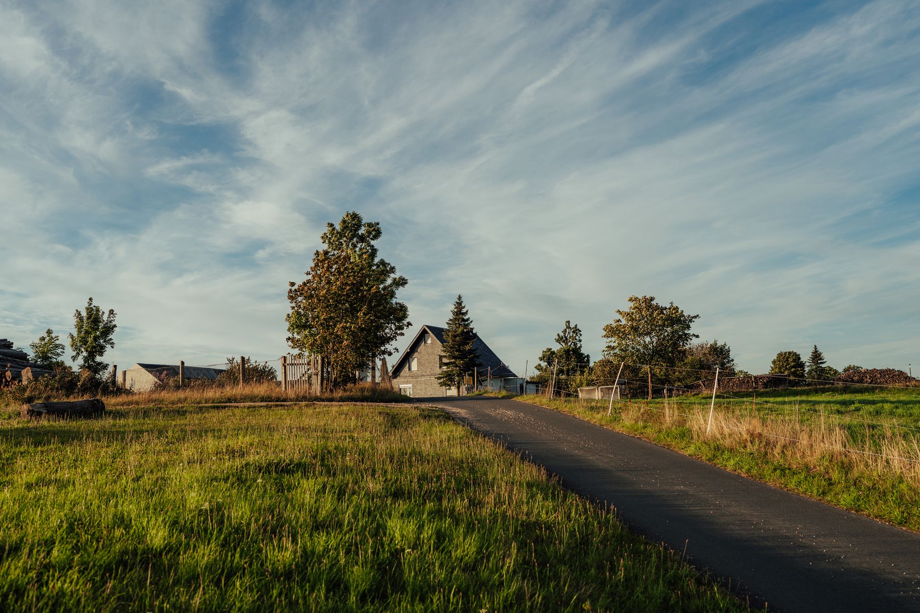 A paved rural driveway leading to a farmhouse