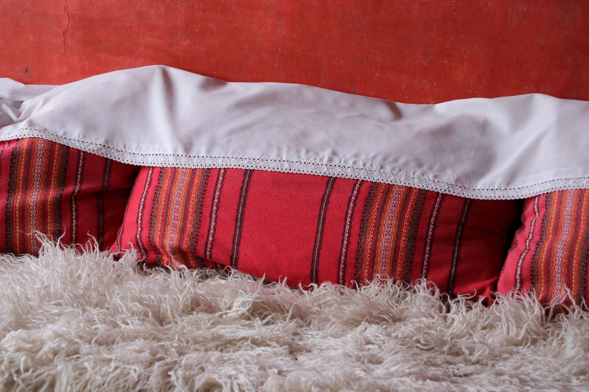 Red pillows and a white blanket on a fluffy rug