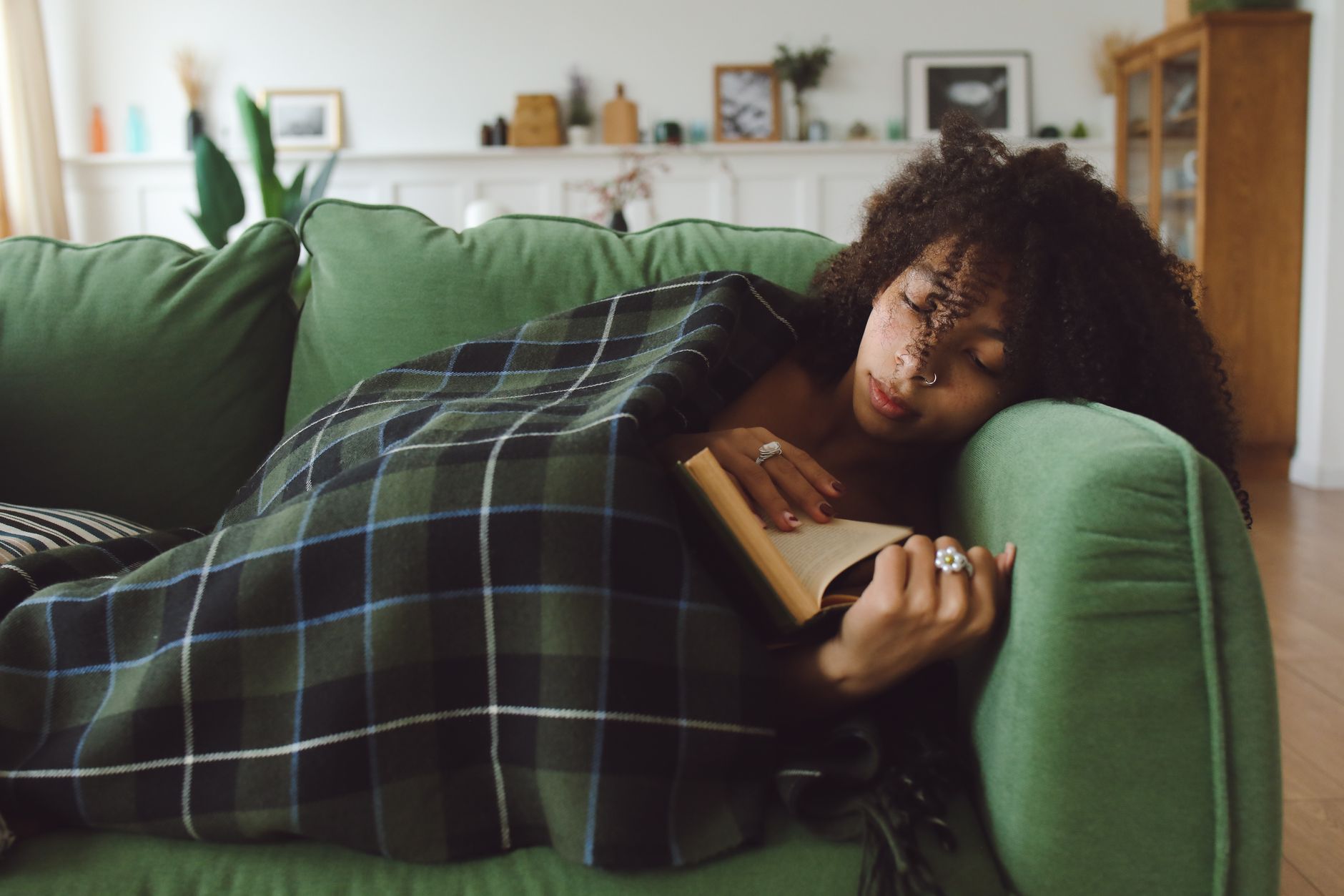 A woman napping under a plaid throw on a sofa