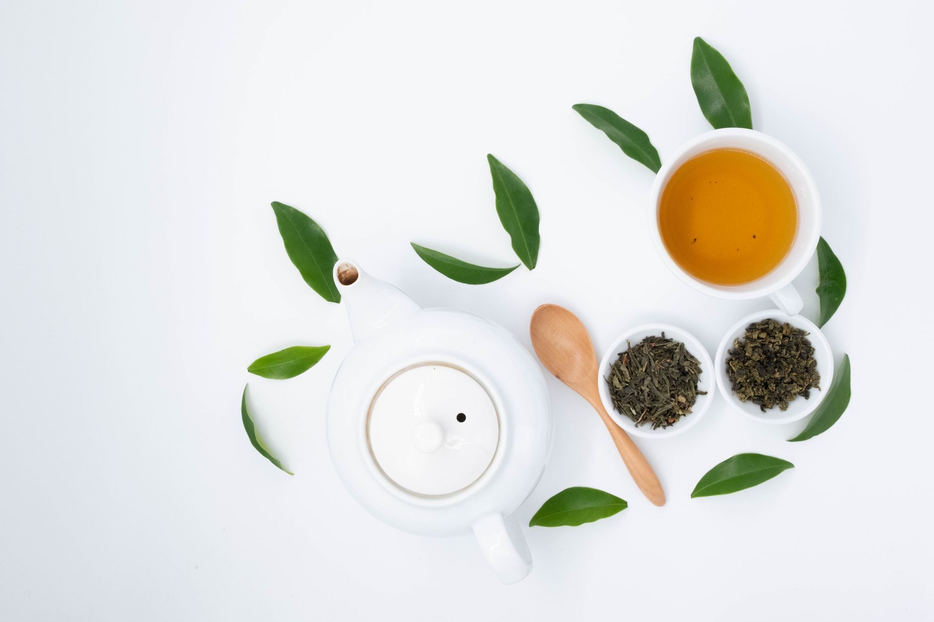 A teapot and loose tea leaves on white