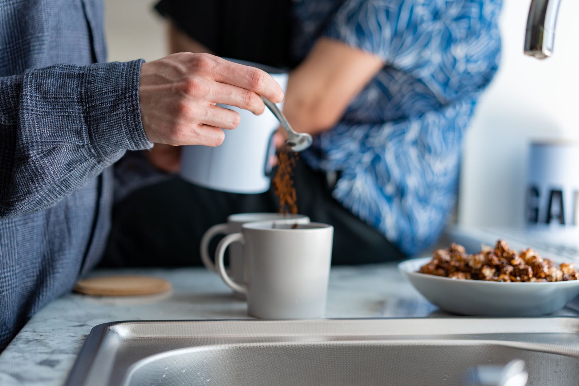 Spooning coffee into a mug by a sink