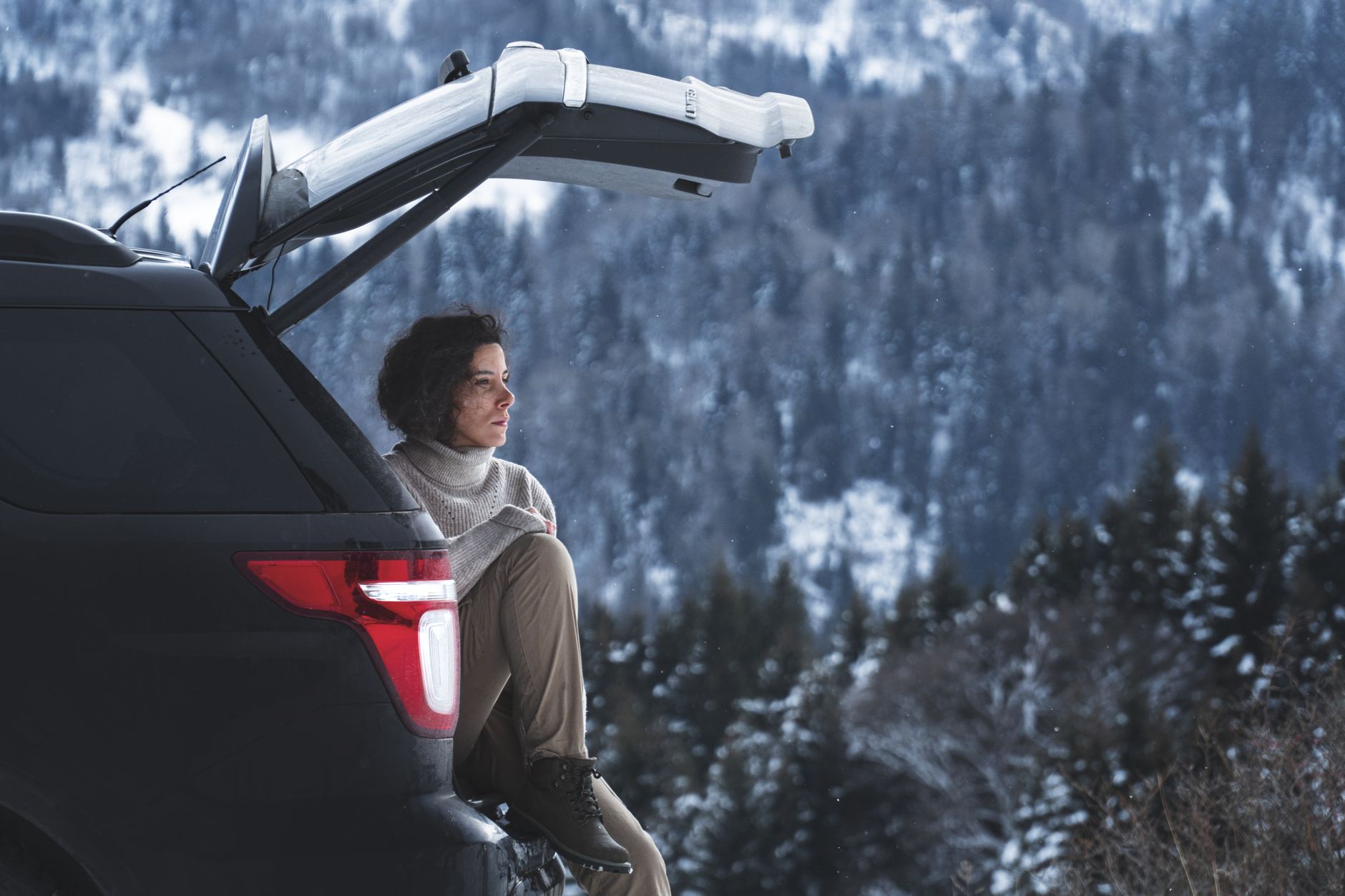 A woman sitting in the open back of an SUV in snowy mountains