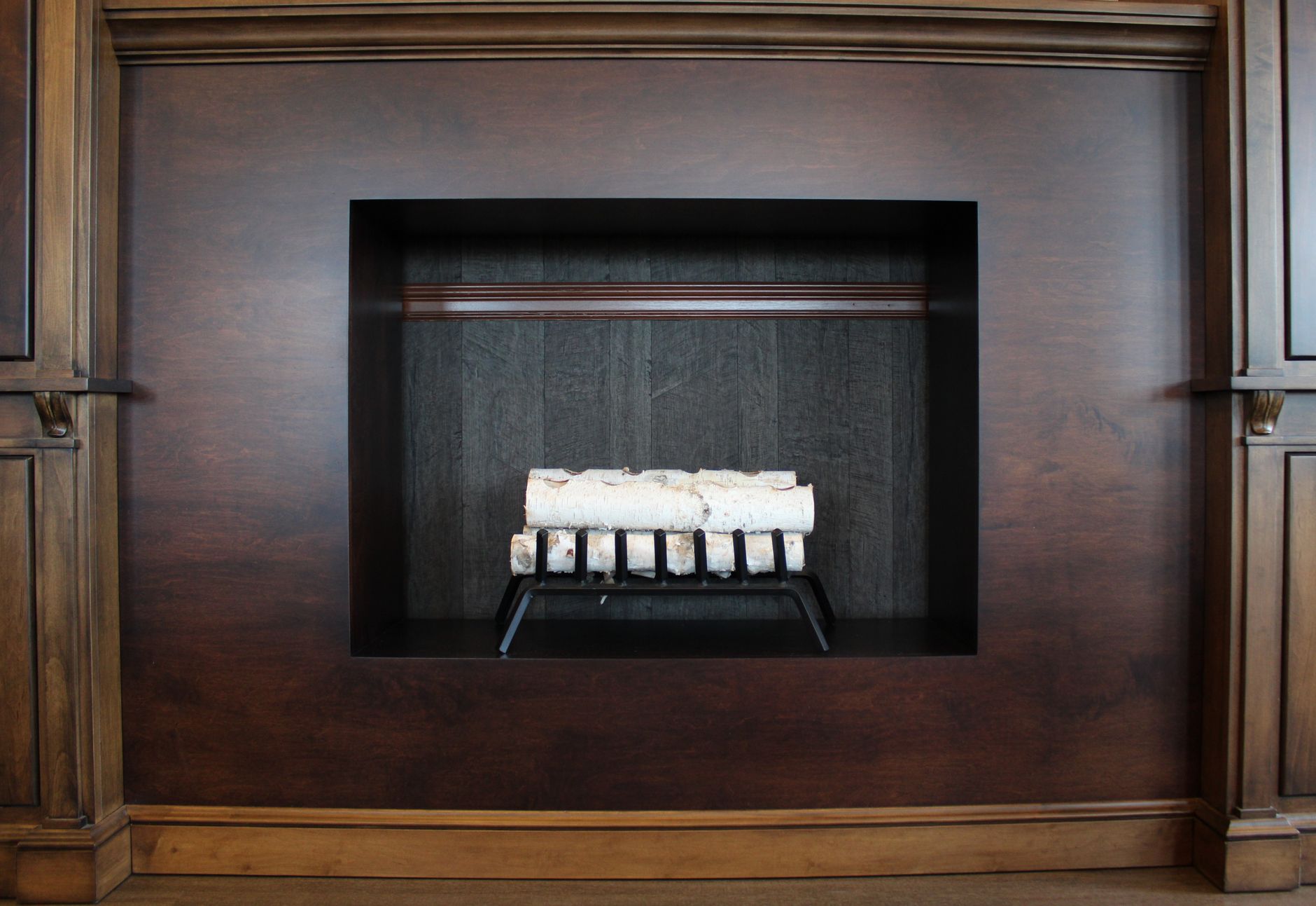 Best fake fireplace logs: birch logs on a grate in a wood-paneled firebox
