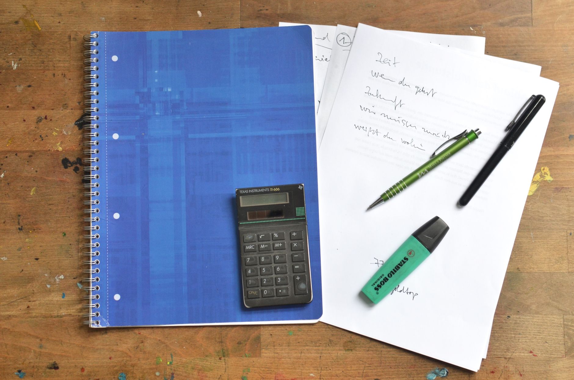 A notebook, calculator and pens on a desk