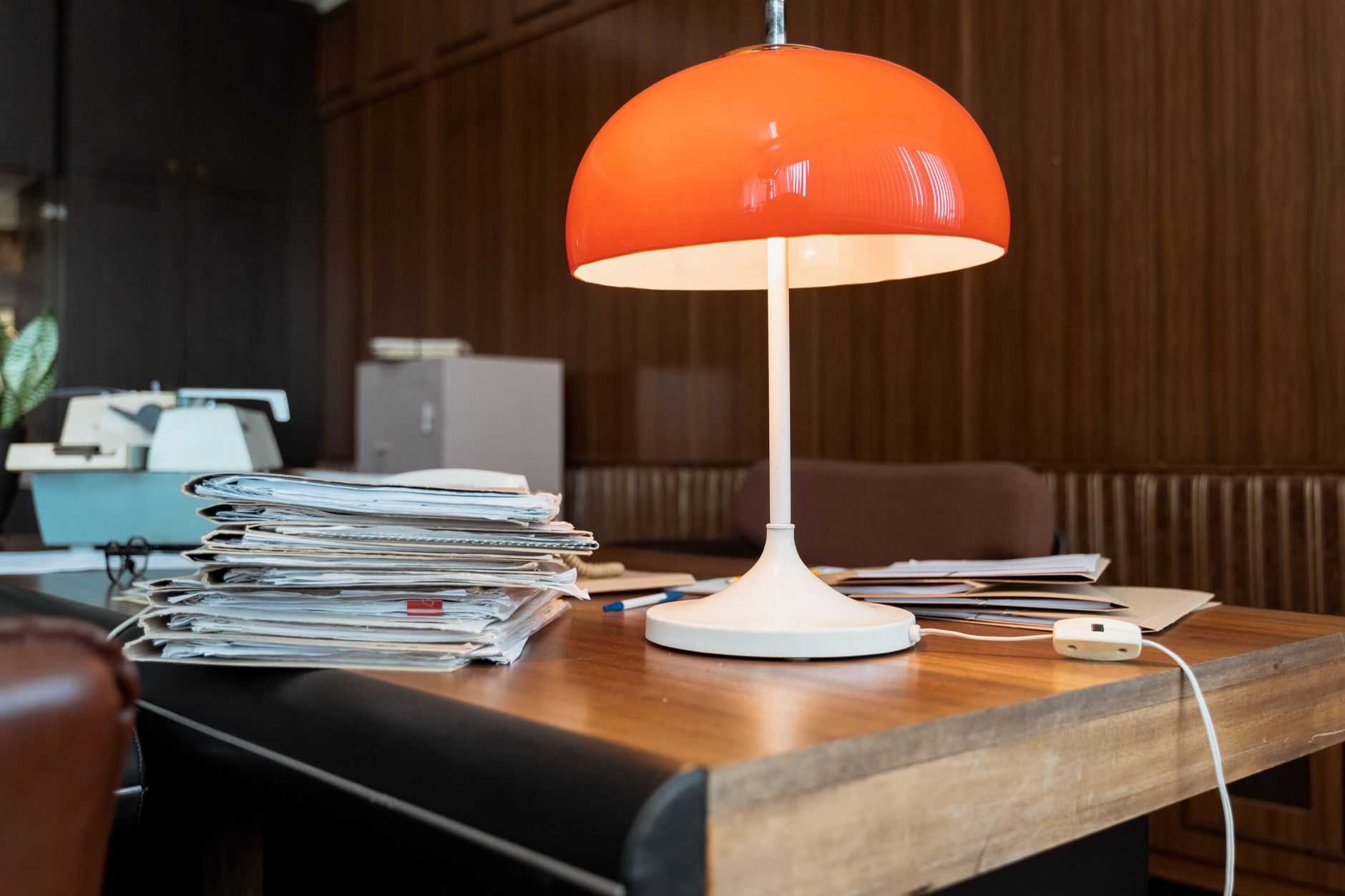 An orange lamp and stacked papers on a desk