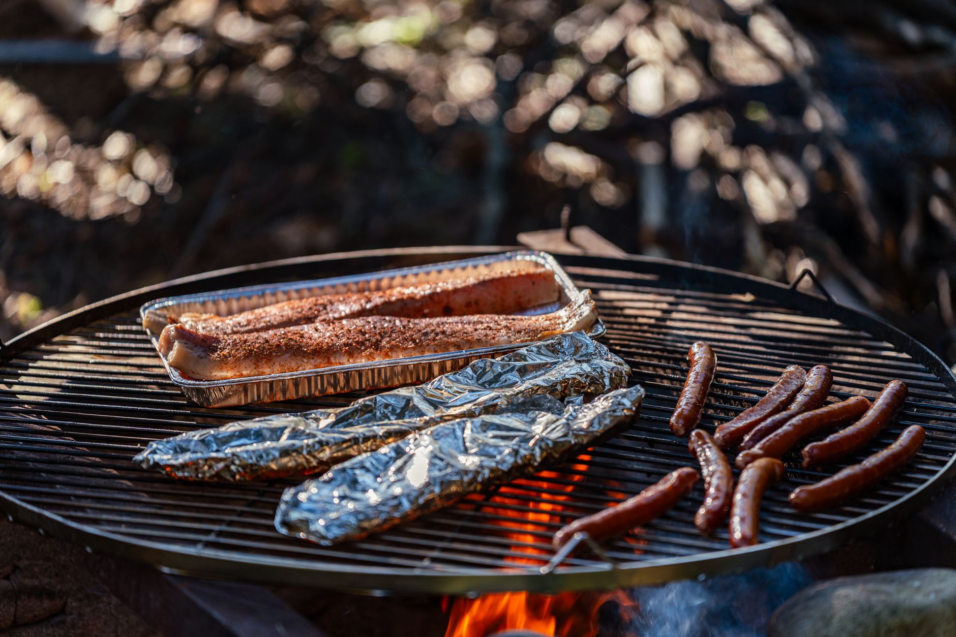 Sausages and foil packets on a fire pit grate