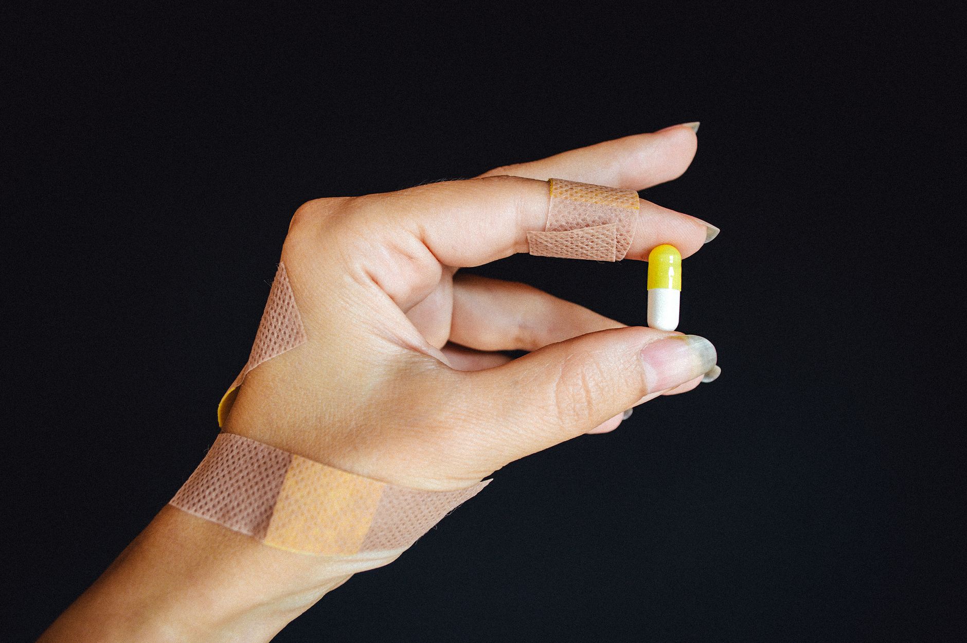 A bandaged hand holding a capsule