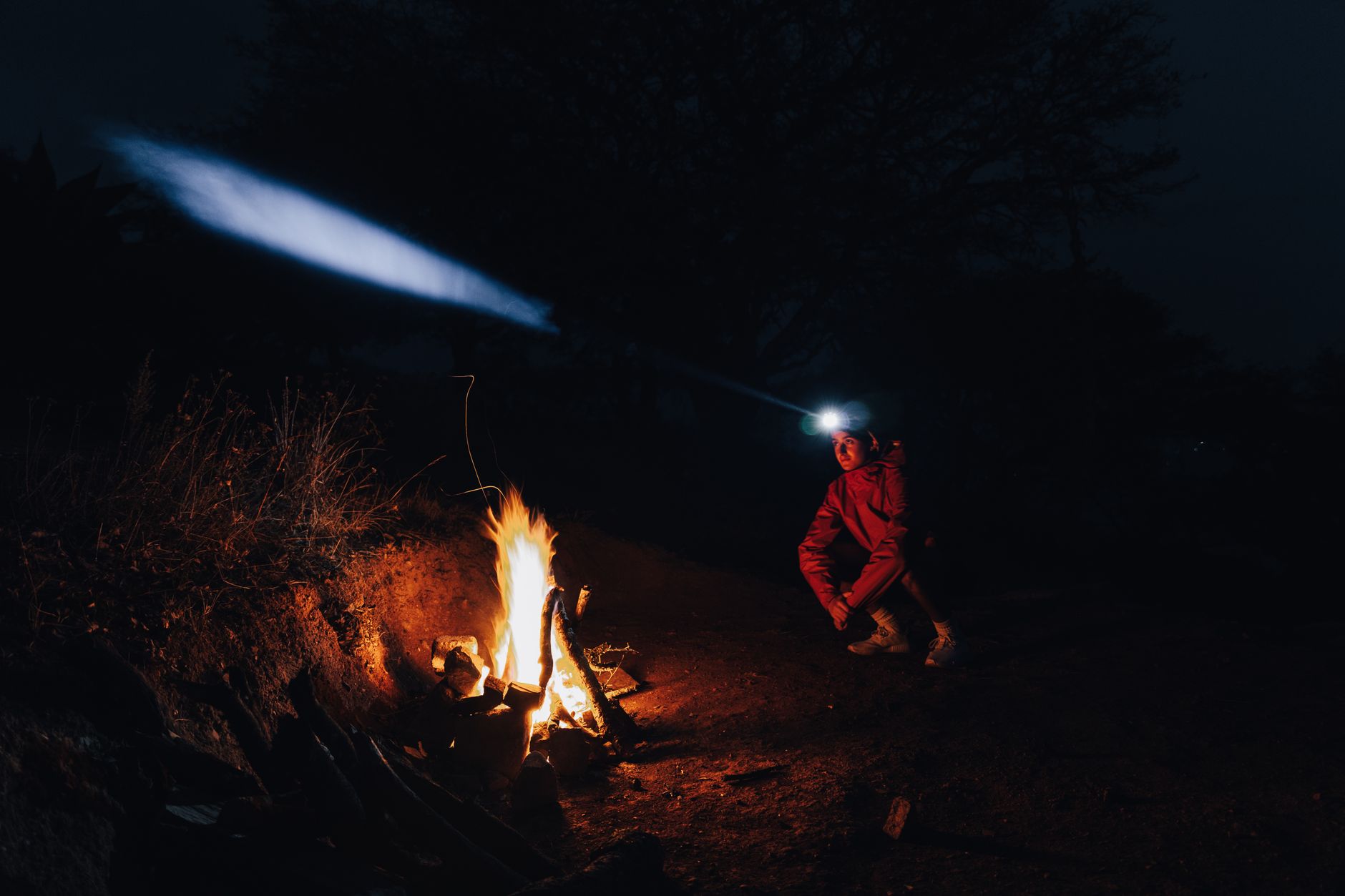 A person wearing a lit headlamp beside a campfire at night