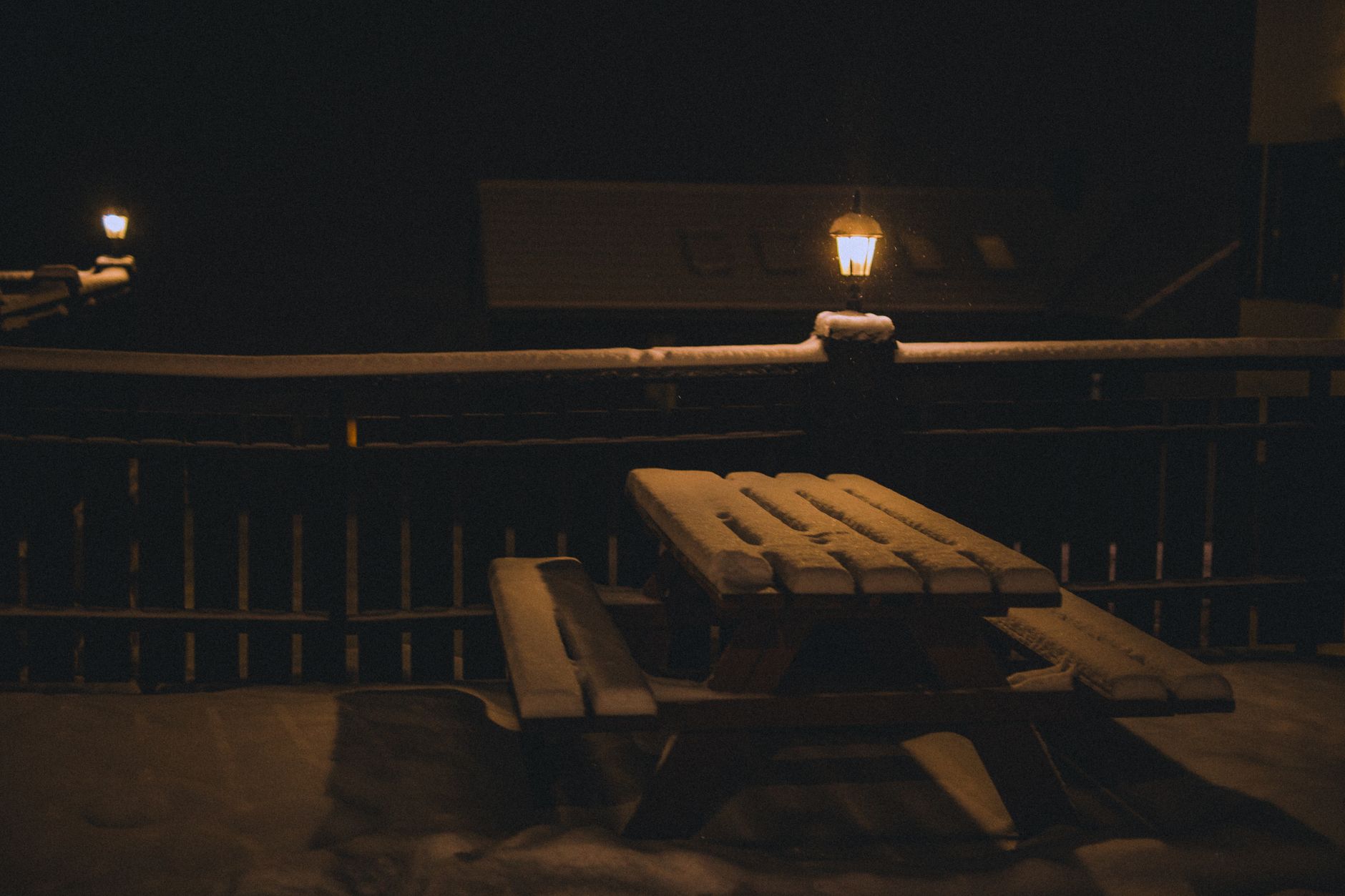 A lamp lighting a snowy picnic table at night