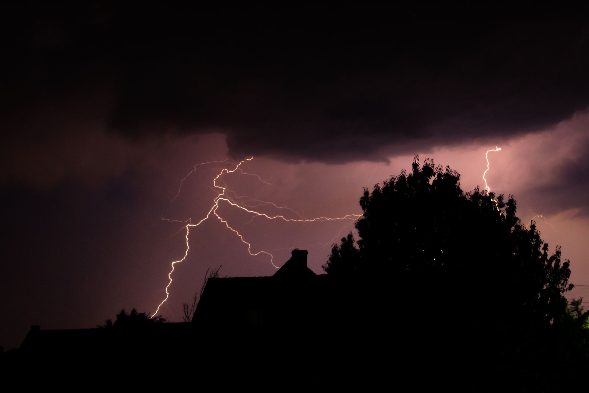 Lightning striking behind a house during a night storm