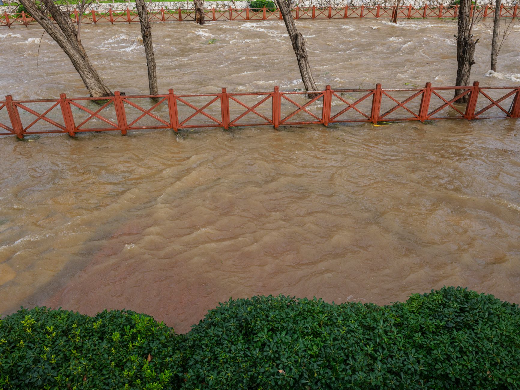 A river over its banks, flooding past a wooden fence