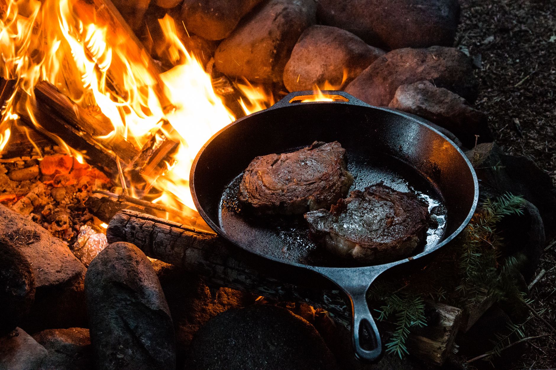 Steaks searing in a cast iron skillet over a campfire