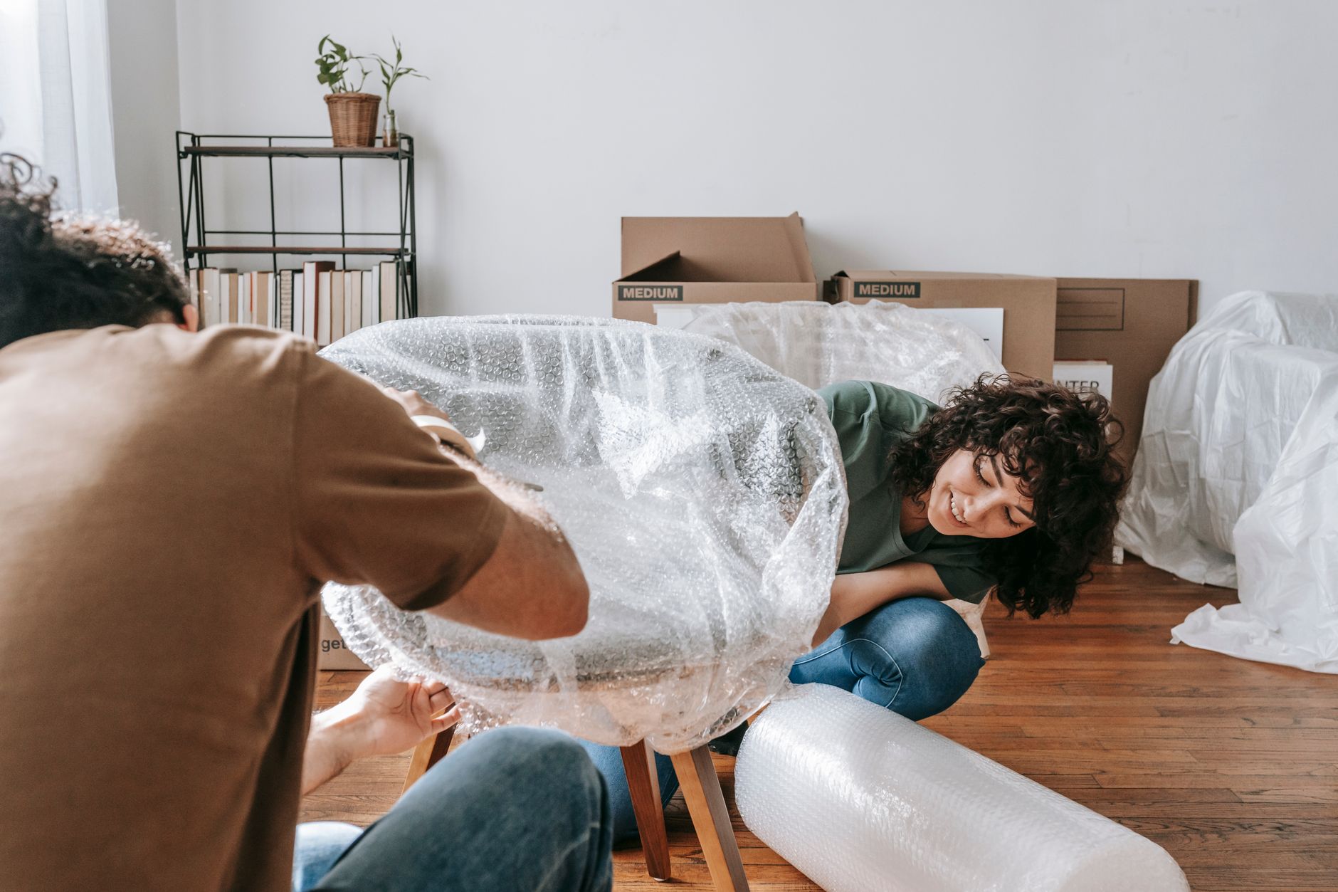 Two people wrapping a chair in plastic for a move