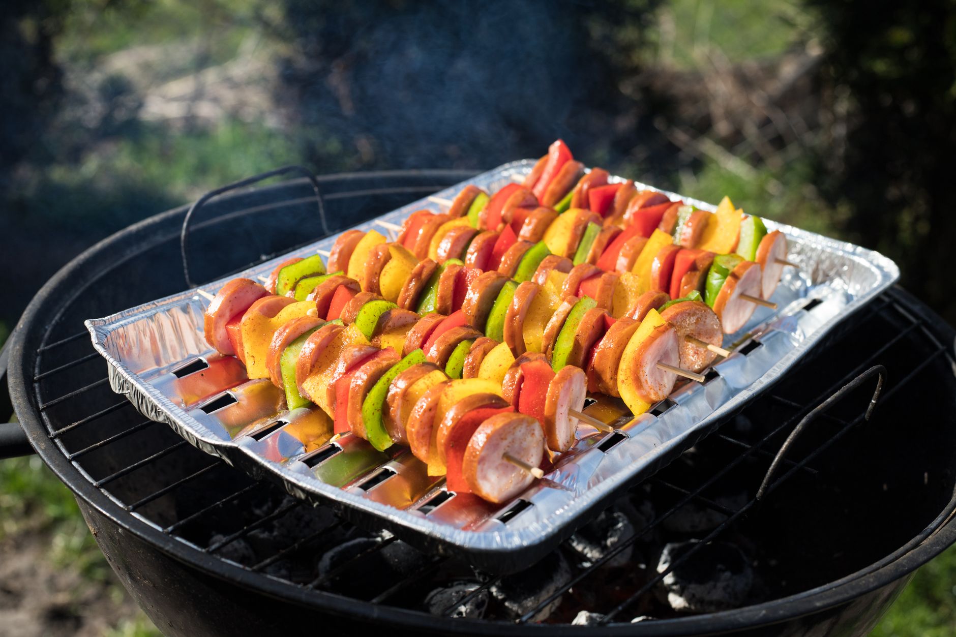 Vegetable skewers in a foil pan on a kettle grill