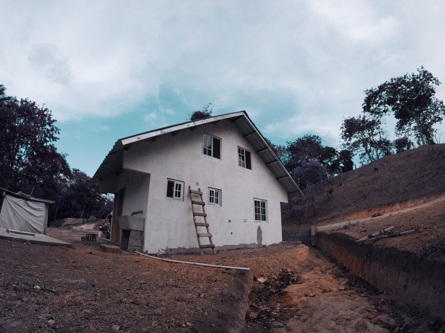 A ladder leaning against a house beside a dirt yard