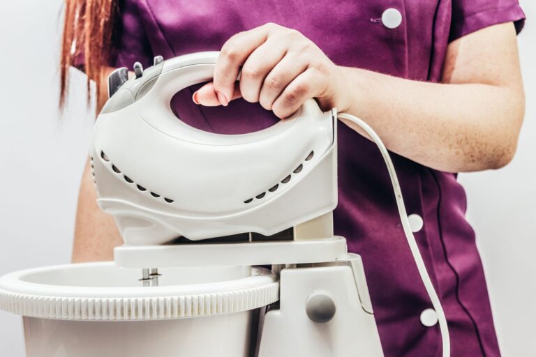 A woman holding a mixer above a bowl