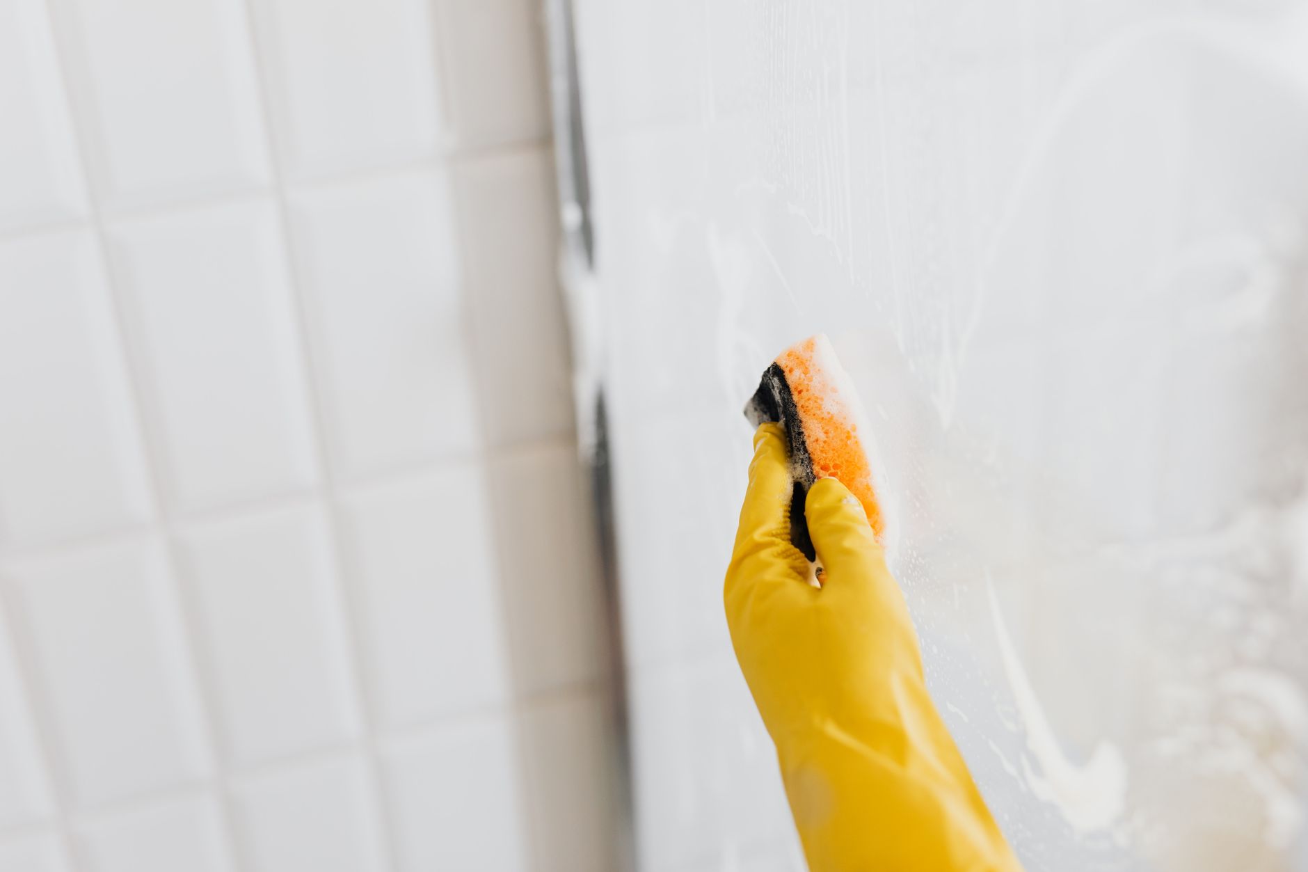 A gloved hand scrubbing shower glass