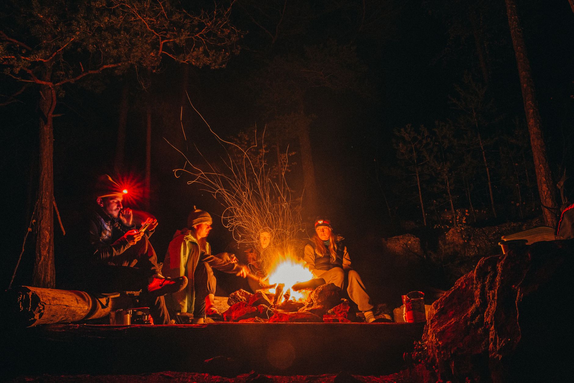 Campers around a fire at night, one wearing a red headlamp