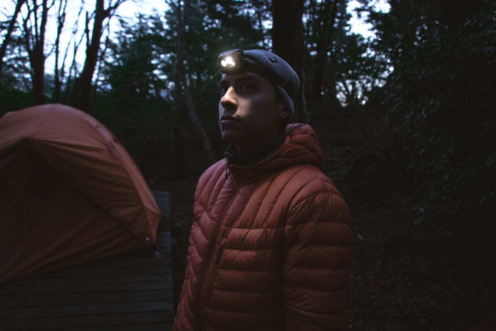 A man wearing a headlamp beside a tent at dusk