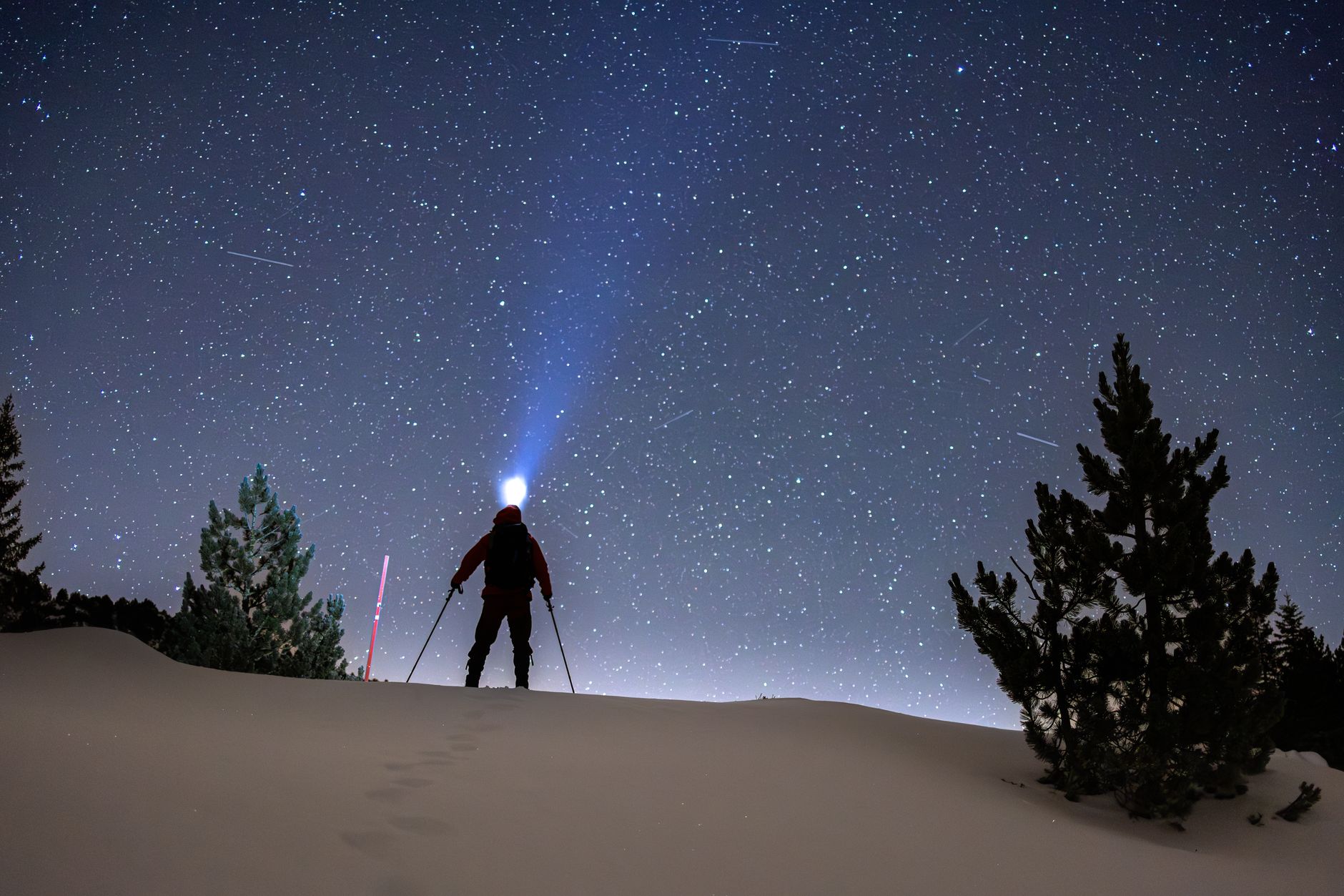 A hiker with a headlamp beam under a starry sky