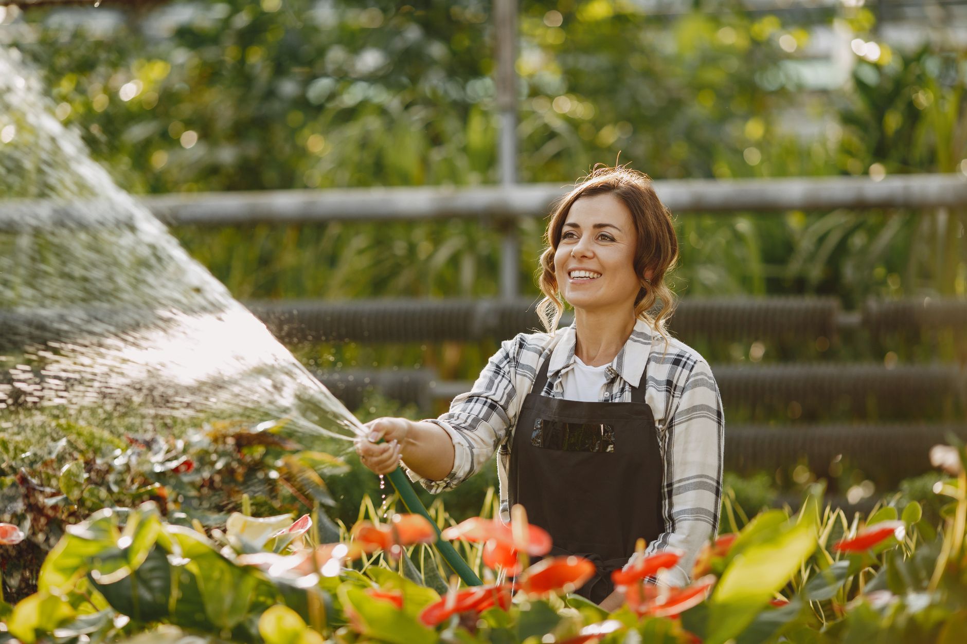 A woman spraying flowers with a garden hose