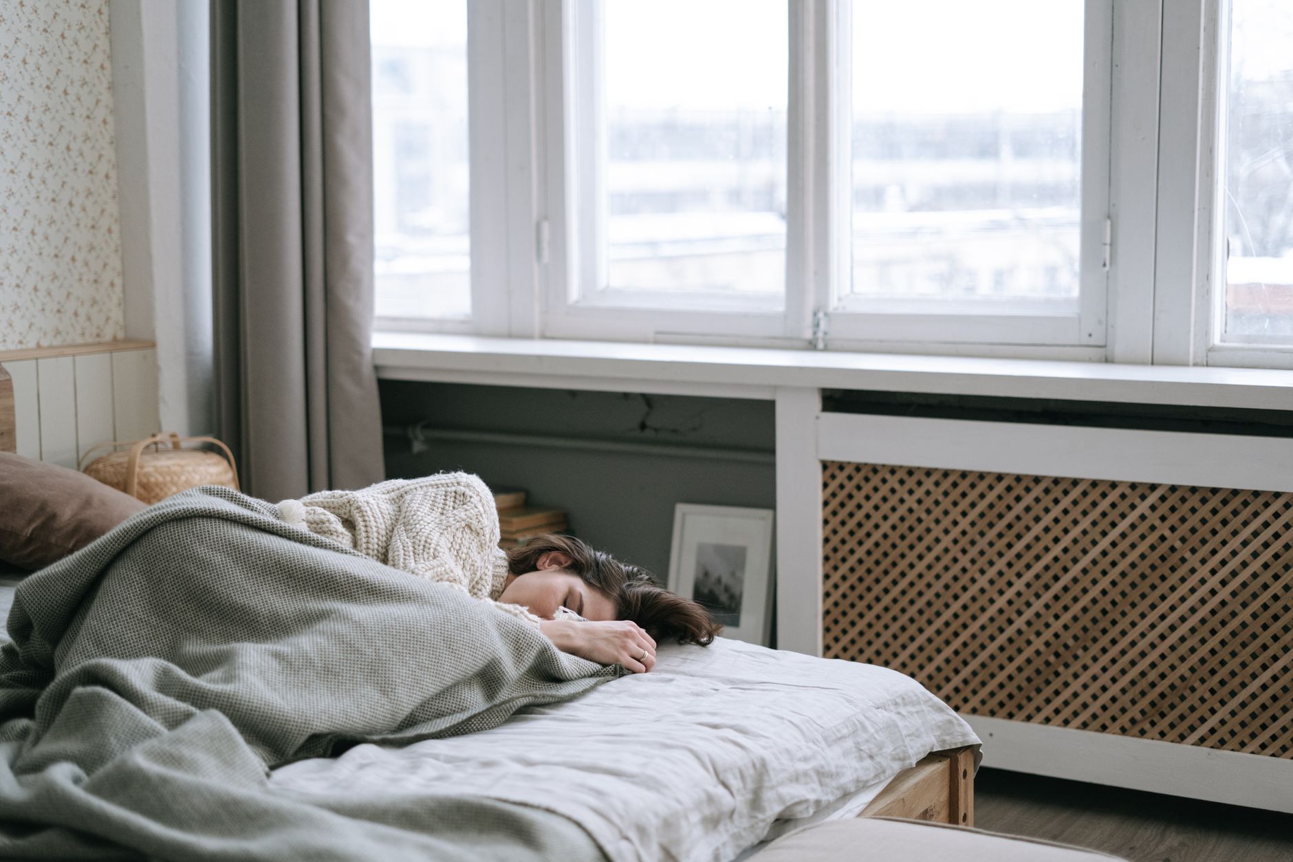 A person sleeping under a blanket in a sunny bedroom